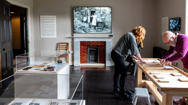 Two people in an exhibition room leaning over a table doing a printing activity.